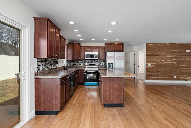 kitchen with tasteful backsplash, appliances with stainless steel finishes, a center island, light wood-style floors, and a sink