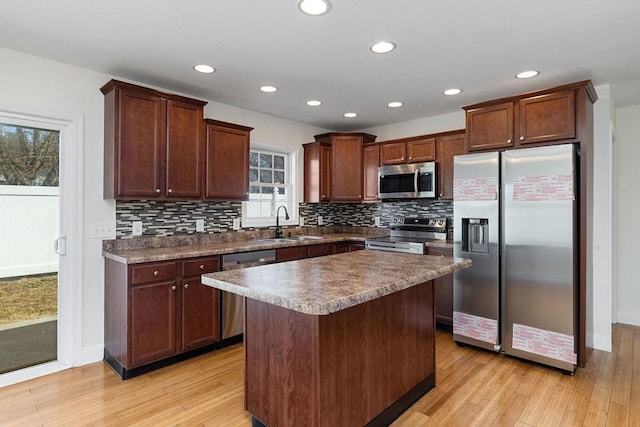 kitchen with light wood finished floors, dark countertops, a kitchen island, appliances with stainless steel finishes, and a sink