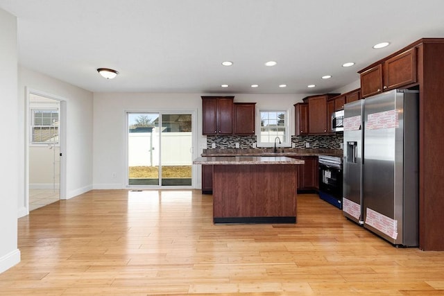 kitchen with light wood-style flooring, a sink, a center island, appliances with stainless steel finishes, and decorative backsplash