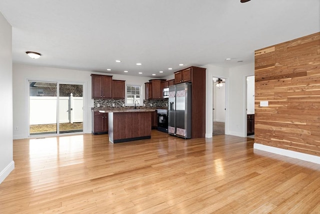 kitchen with a ceiling fan, a kitchen island, appliances with stainless steel finishes, light wood-style floors, and backsplash