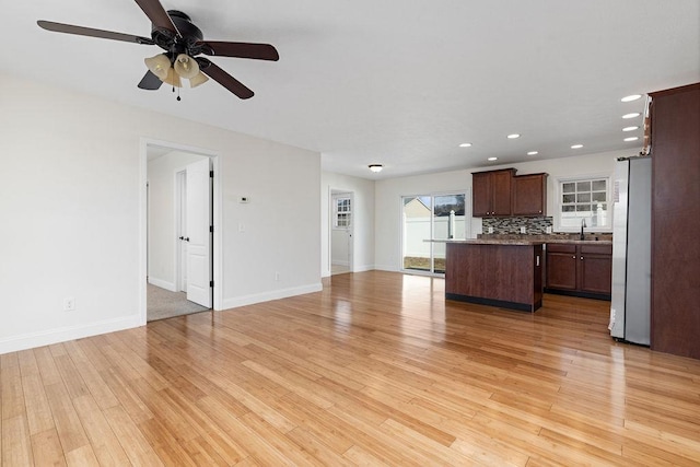 unfurnished living room with light wood-style floors, a sink, and baseboards