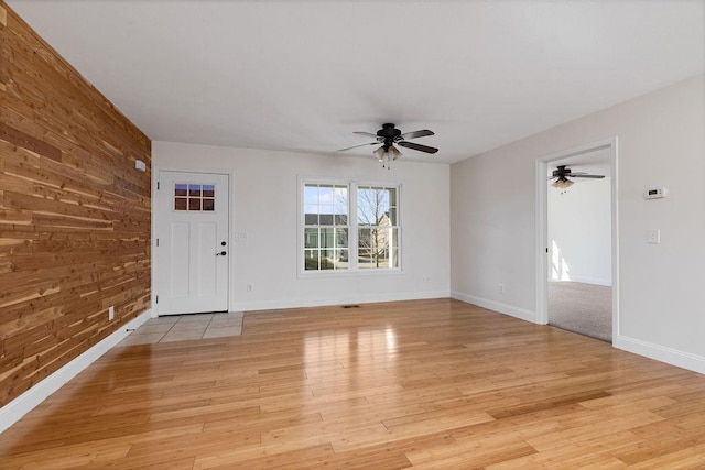 interior space featuring a ceiling fan, light wood-type flooring, wood walls, and baseboards