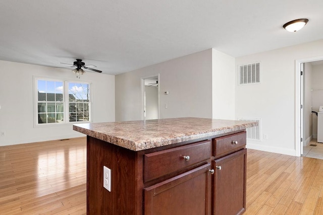 kitchen with light wood finished floors, a ceiling fan, visible vents, and a center island