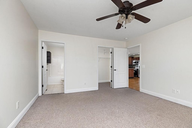 unfurnished bedroom with baseboards, a ceiling fan, light colored carpet, ensuite bathroom, and a spacious closet