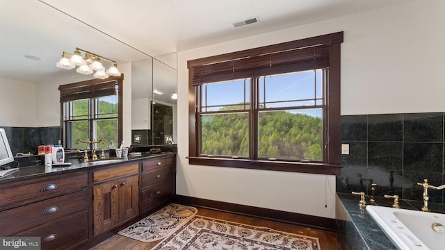 bathroom with tiled tub, vanity, and wood-type flooring