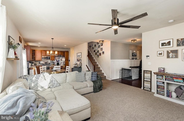 living area with stairs, ceiling fan with notable chandelier, dark colored carpet, a fireplace, and recessed lighting