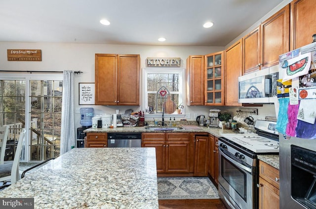 kitchen featuring appliances with stainless steel finishes, glass insert cabinets, and light stone countertops