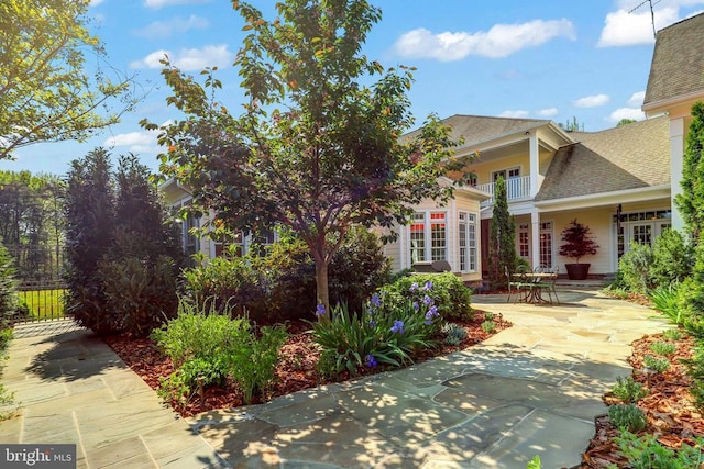 view of front of house featuring roof with shingles, a patio, and a balcony