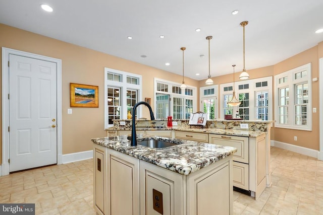 kitchen with sink, hanging light fixtures, light stone countertops, a center island with sink, and cream cabinetry