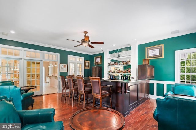 bar featuring ornamental molding, wainscoting, ceiling fan, a dry bar, and dark wood finished floors
