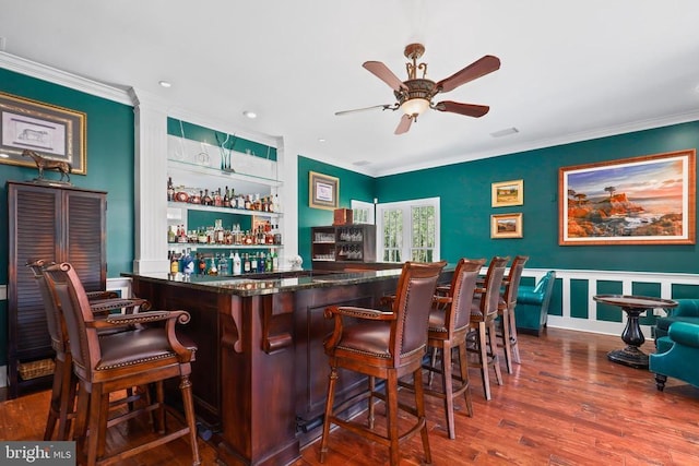 bar featuring ceiling fan, crown molding, a dry bar, wood finished floors, and a wainscoted wall