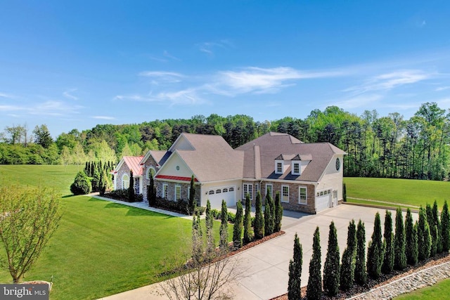 view of front facade with an attached garage, a front lawn, stone siding, concrete driveway, and a forest view