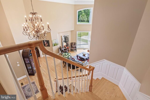 stairs with hardwood / wood-style floors, a towering ceiling, and a notable chandelier