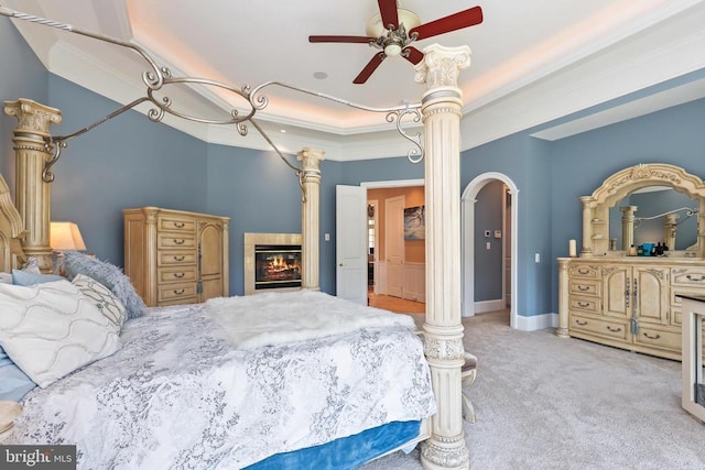 bedroom featuring a ceiling fan, crown molding, a raised ceiling, carpet floors, and a glass covered fireplace