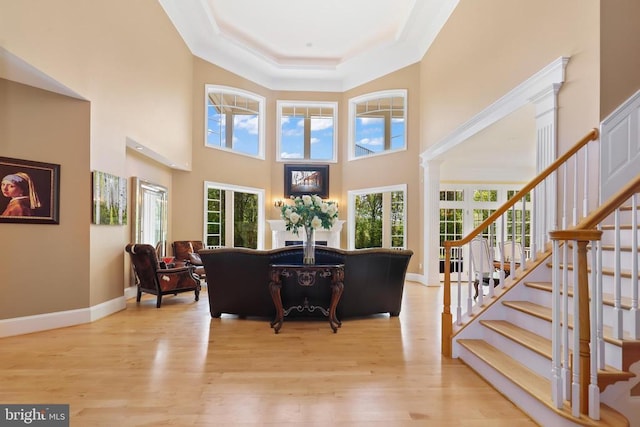 living room featuring a towering ceiling, wood finished floors, stairway, baseboards, and a raised ceiling