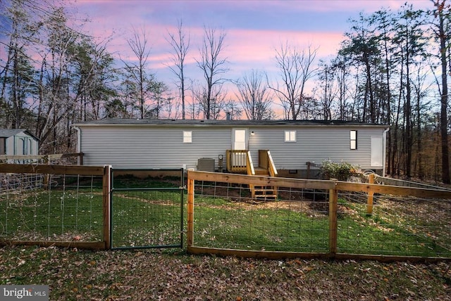 back of house at dusk with crawl space, a lawn, fence, and a gate