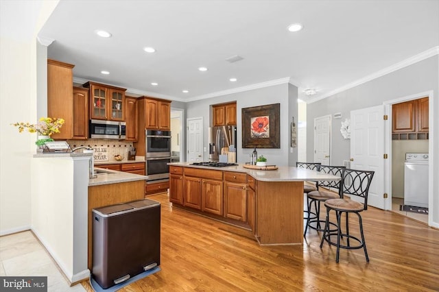 kitchen with washer / dryer, a kitchen breakfast bar, light countertops, stainless steel appliances, and backsplash