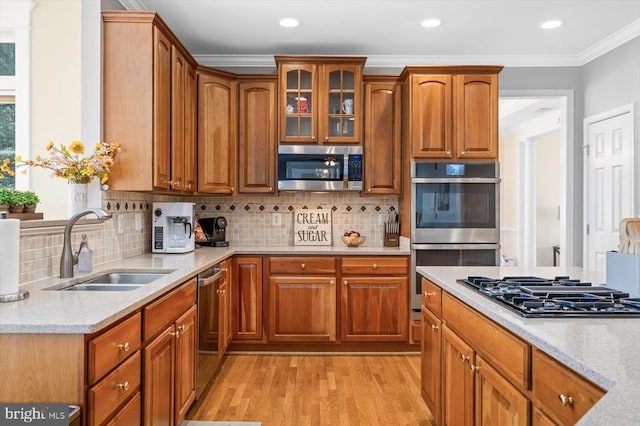 kitchen featuring light wood-style flooring, appliances with stainless steel finishes, glass insert cabinets, ornamental molding, and a sink