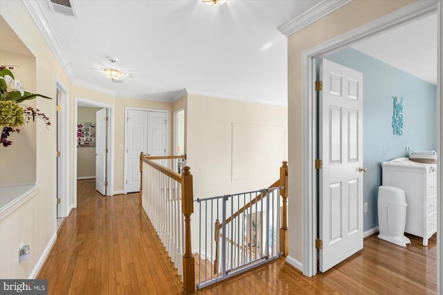 hall with visible vents, baseboards, an upstairs landing, light wood finished floors, and crown molding