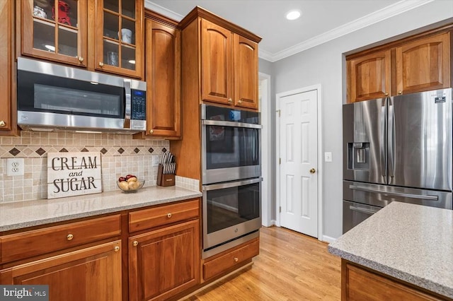 kitchen with appliances with stainless steel finishes, backsplash, glass insert cabinets, and crown molding