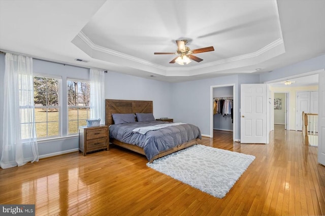 bedroom with a tray ceiling, baseboards, visible vents, and light wood finished floors