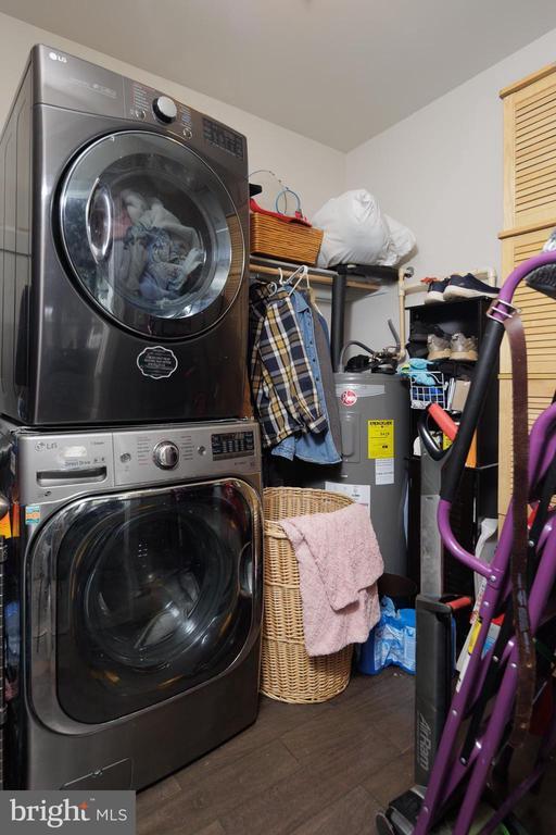 clothes washing area featuring stacked washer and dryer, water heater, laundry area, and wood finished floors