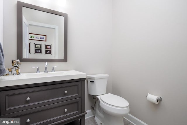 half bathroom featuring baseboards, vanity, and toilet