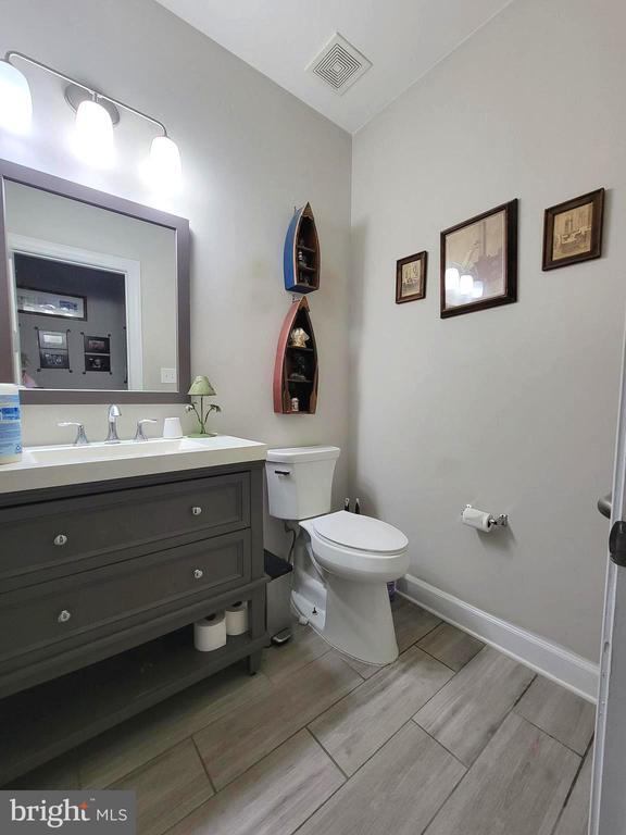 half bath with baseboards, visible vents, toilet, vanity, and wood finish floors