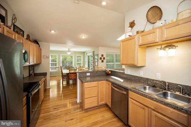 kitchen featuring light brown cabinetry, a sink, a peninsula, light wood-style floors, and stainless steel appliances