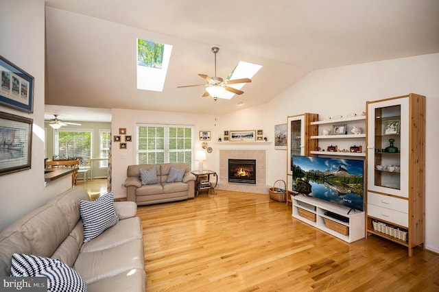 living room with lofted ceiling with skylight, wood finished floors, ceiling fan, and a tile fireplace