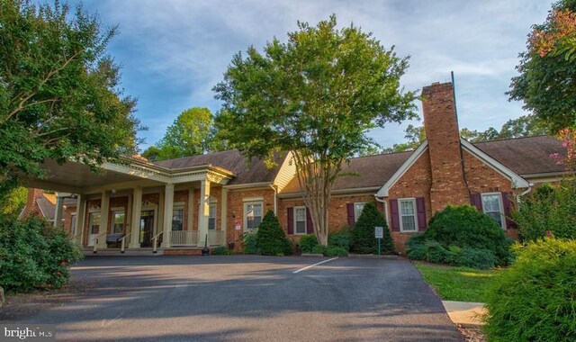 view of front of house featuring covered porch, a chimney, and brick siding