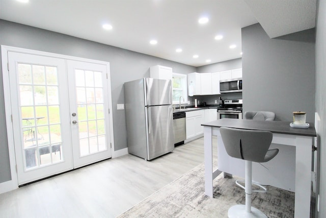 kitchen with sink, stainless steel appliances, white cabinets, french doors, and light wood-type flooring