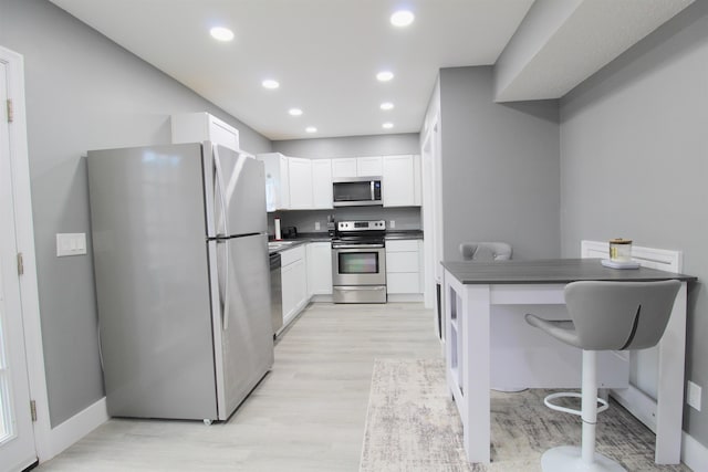 kitchen with light wood-type flooring, a breakfast bar, white cabinets, and appliances with stainless steel finishes