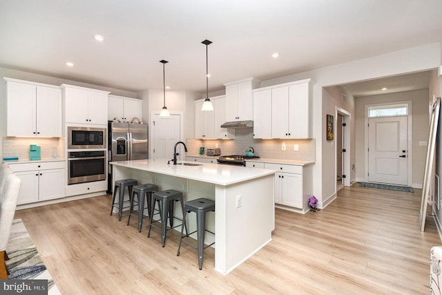 kitchen with a breakfast bar, light wood-style floors, backsplash, and appliances with stainless steel finishes