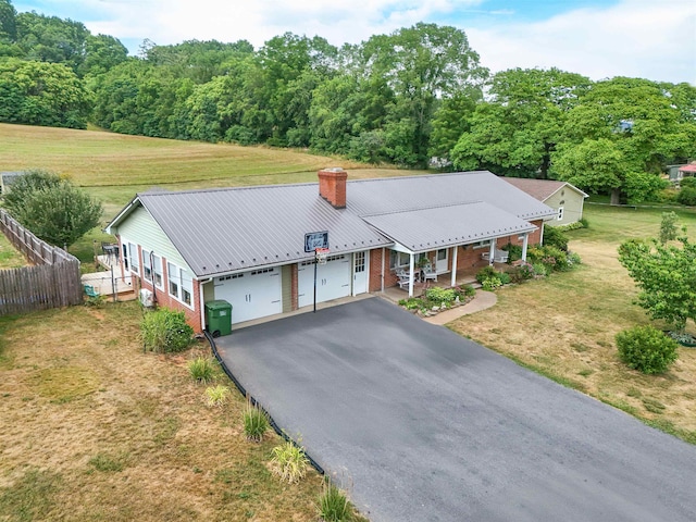 ranch-style house featuring metal roof, a porch, aphalt driveway, brick siding, and fence