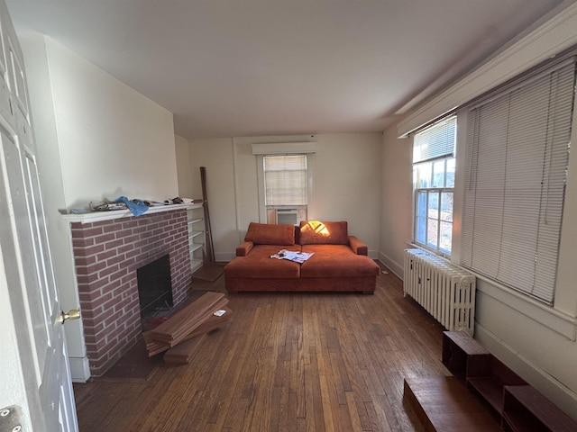 living area with radiator heating unit, dark hardwood / wood-style floors, and a brick fireplace