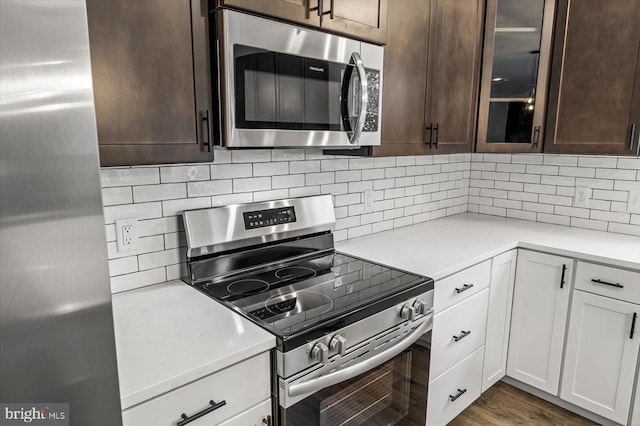 kitchen with white cabinets, decorative backsplash, glass insert cabinets, stainless steel appliances, and light countertops