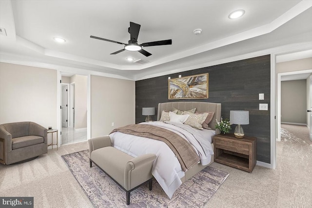 bedroom with wooden walls, an accent wall, a raised ceiling, and light colored carpet