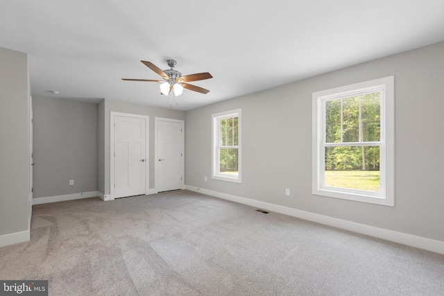 unfurnished bedroom featuring multiple closets, light colored carpet, and ceiling fan