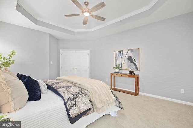 carpeted bedroom featuring baseboards, a tray ceiling, ceiling fan, ornamental molding, and a closet