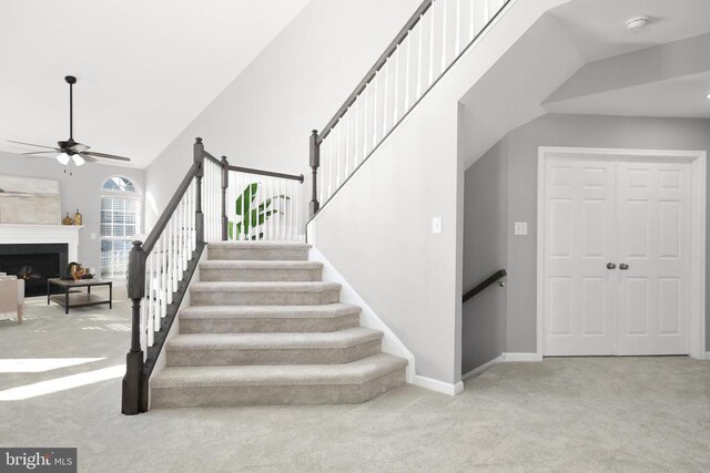 stairs featuring baseboards, carpet, a fireplace, and a ceiling fan