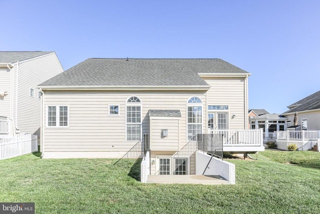 rear view of property featuring a yard, roof with shingles, and a deck