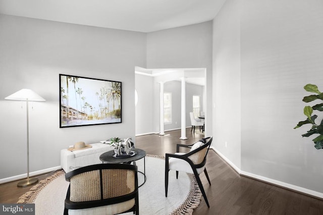 living area featuring decorative columns, wood finished floors, and baseboards