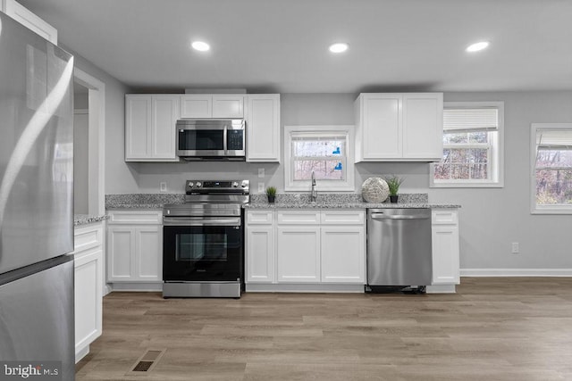 kitchen featuring stainless steel appliances, white cabinets, a sink, and light stone counters