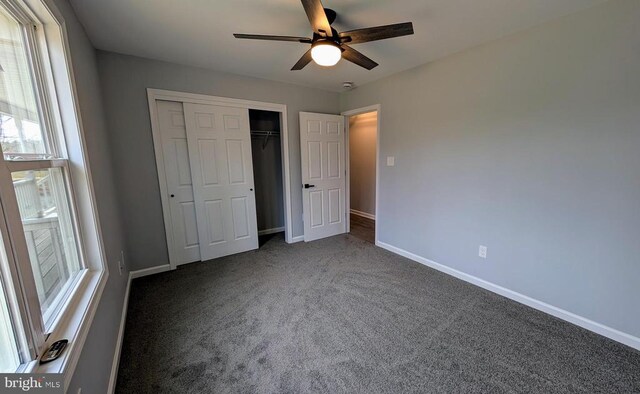 unfurnished bedroom with ceiling fan, dark carpet, and a closet