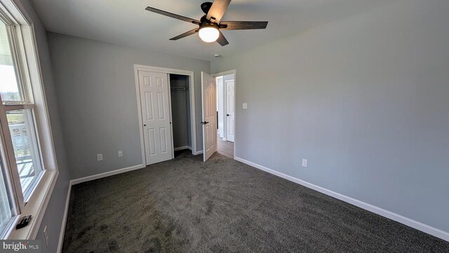 unfurnished bedroom with ceiling fan, a closet, and dark colored carpet