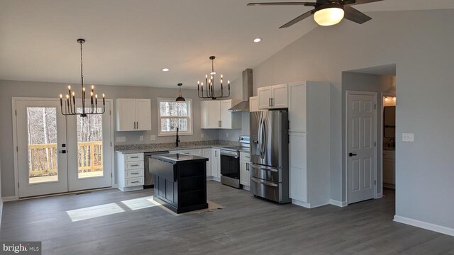 kitchen featuring appliances with stainless steel finishes, white cabinetry, hanging light fixtures, a center island, and wall chimney exhaust hood