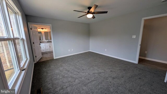 unfurnished bedroom featuring ceiling fan, ensuite bathroom, and dark colored carpet