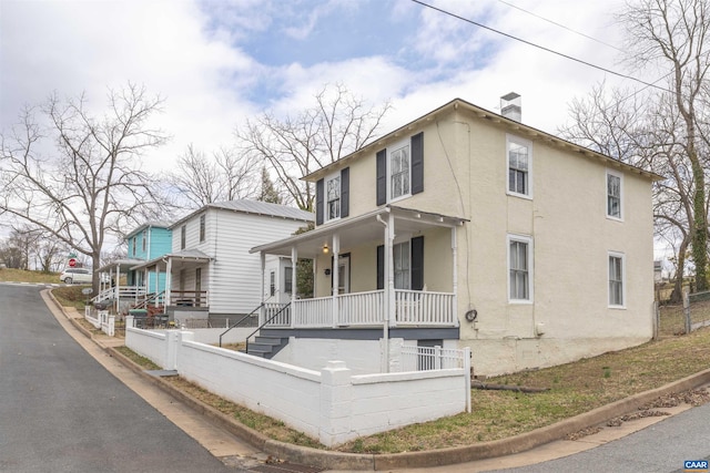 view of front of home with a fenced front yard, covered porch, a chimney, and stucco siding