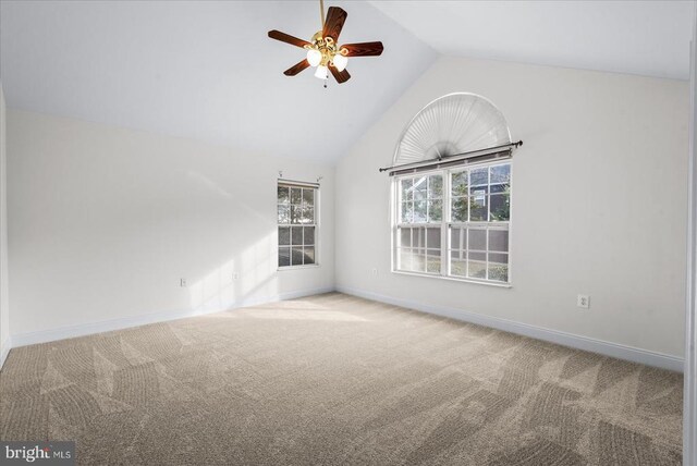 carpeted empty room featuring a ceiling fan, vaulted ceiling, and baseboards